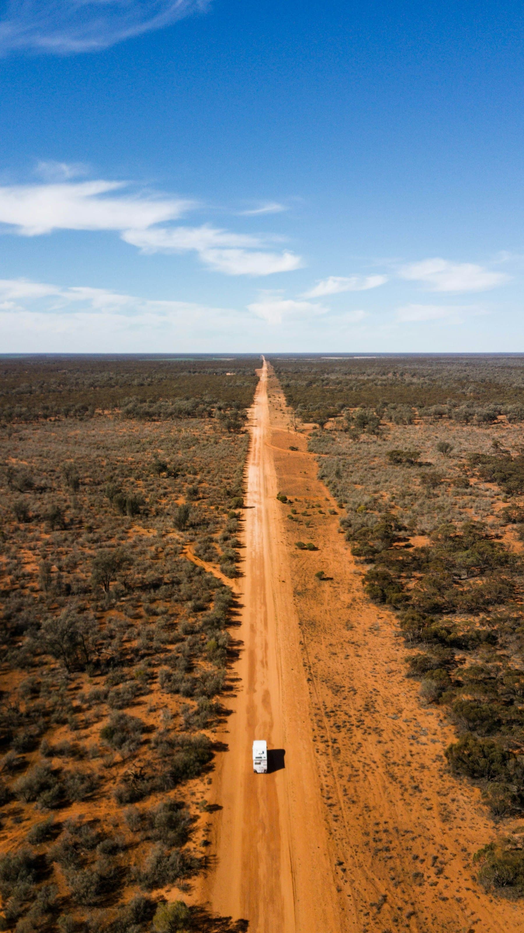 Aerial view of a vehicle on a long straight red dirt road through the outback.