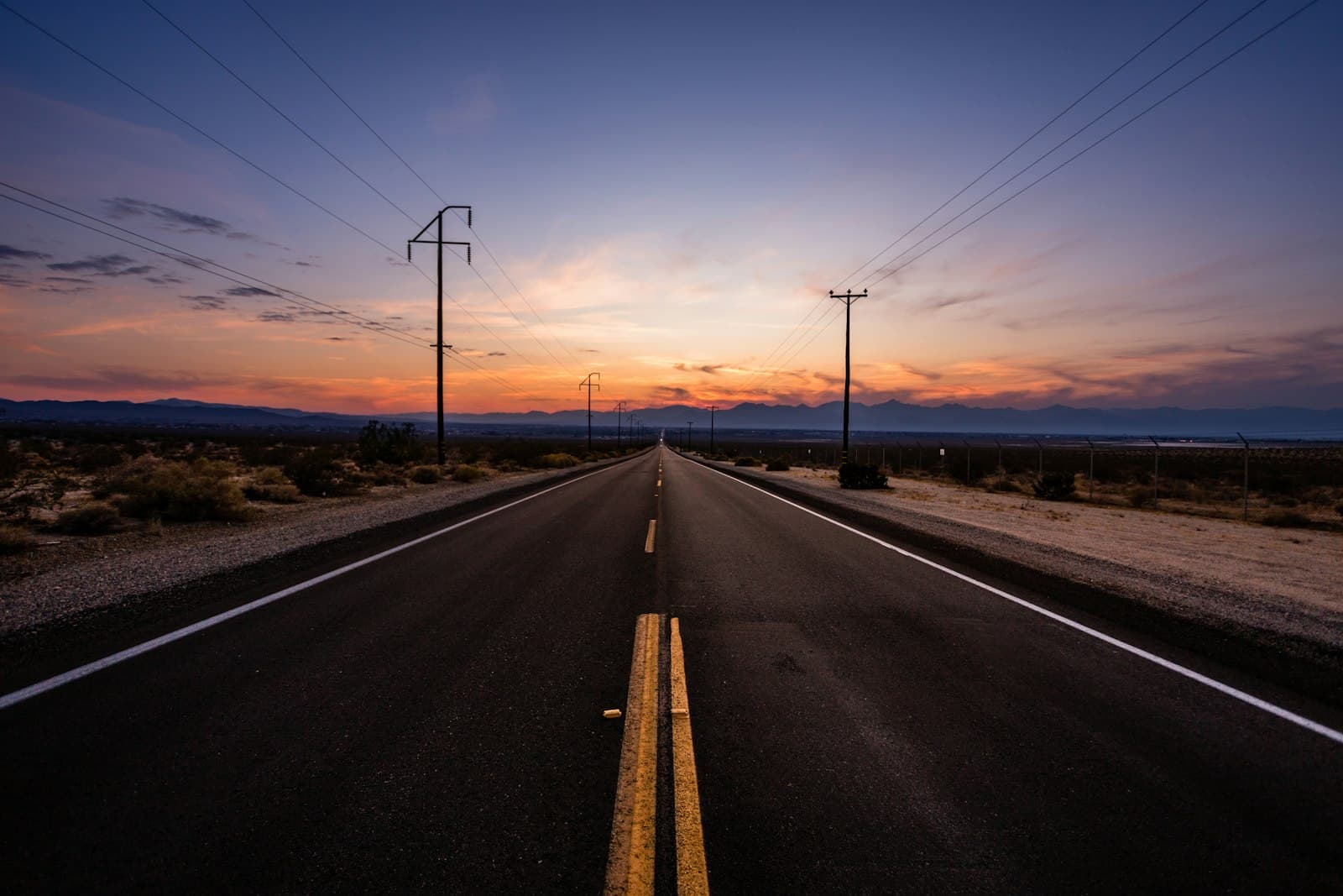 A long open road heading into an outback sunset.